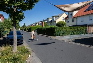 Ein Mann steht auf einem Laufband, welches in der Mitte einer kleinen Nebenstraße in einer Wohnsiedlung steht.
