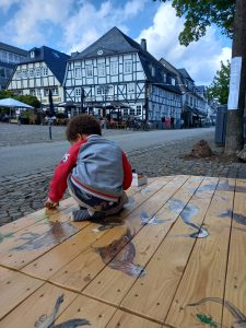 Ein Kind spielt auf einer mit Tieren bemalten Holzplattform in der Briloner Innenstadt.