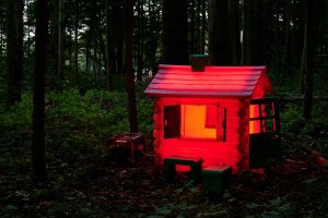 Die Spielzeughütte besteht aus Kunststoff. Sie leuchtet rot. Im Wald ist es dunkel.