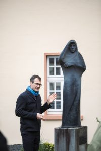 Thomas Geiger steht neben einer Bronzestatue und erzählt.