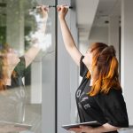 Eine Künstlerin malt mit einem Edding-Stift etwas auf eine Schaufensterfassade.