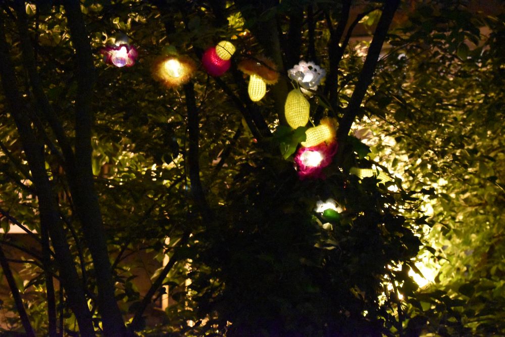 Ein Baum bei Nacht. in dem mehrere gehäkelte, beleuchtete Objekte hängen.