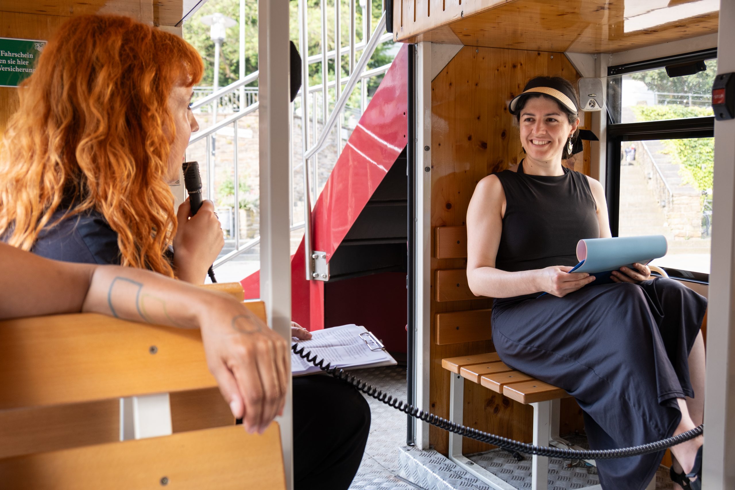 Zwei Frauen sitzen einander in einem alten Doppeldecker-Bus gegenüber und unterhalten sich.