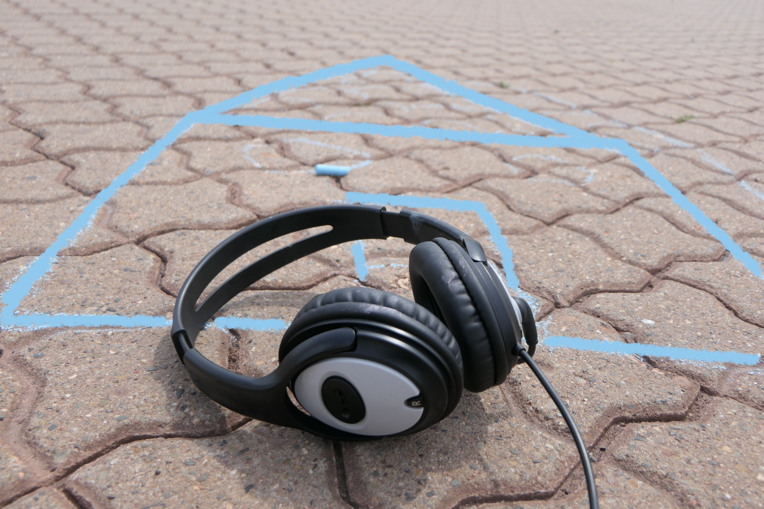 Overear-Kopfhörer mit Kabel auf Asphalt mit blauer Kreidezeichnung.