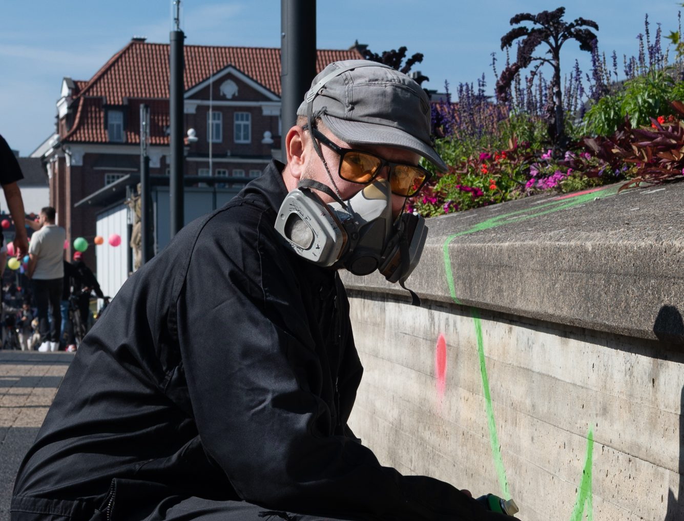 Ein Mann mit Atemschutz kniet vor einer kleinen Mauer und schaut in die Kamera.