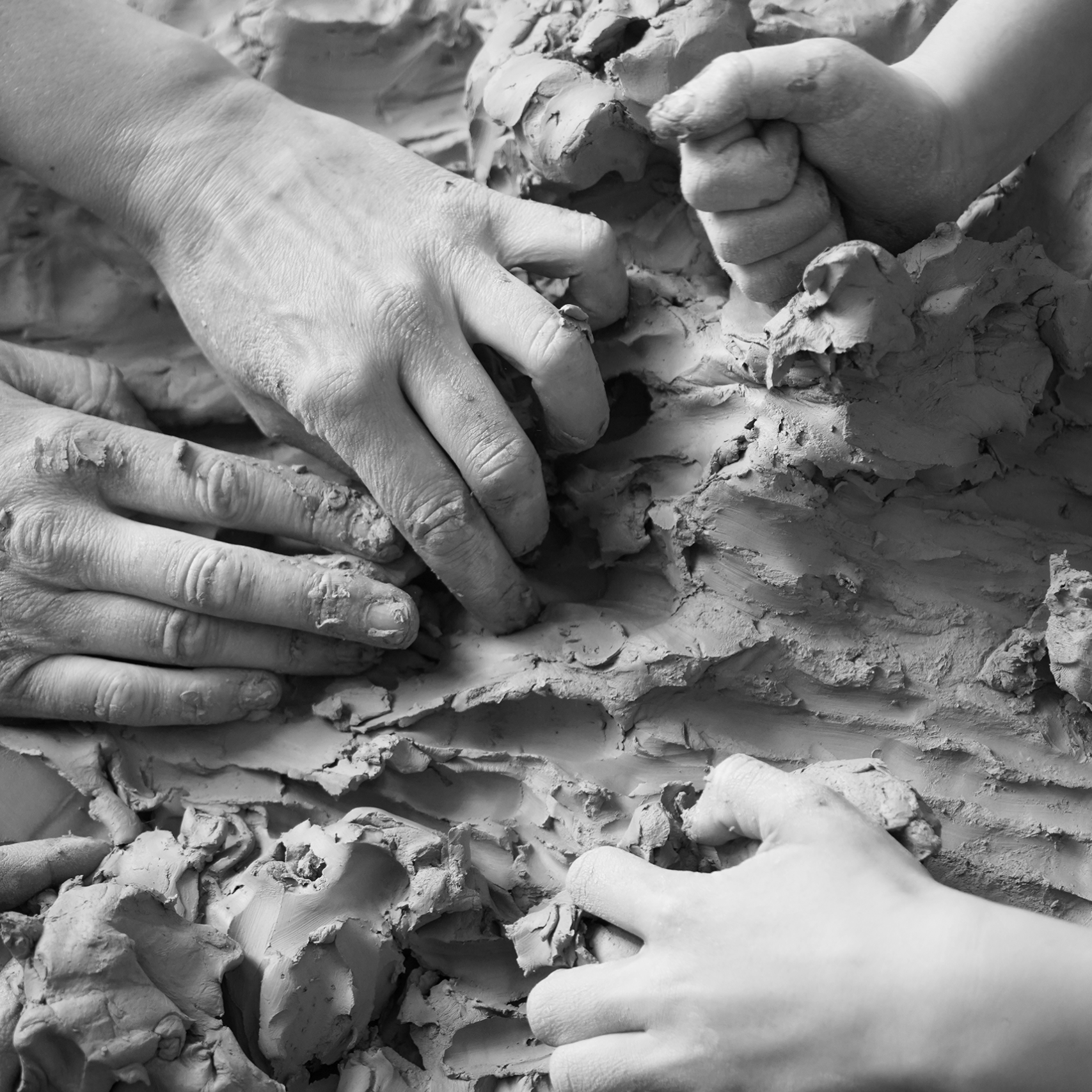 Schwarz-weiß Bild mehrerer Hände, die in Ton greifen.